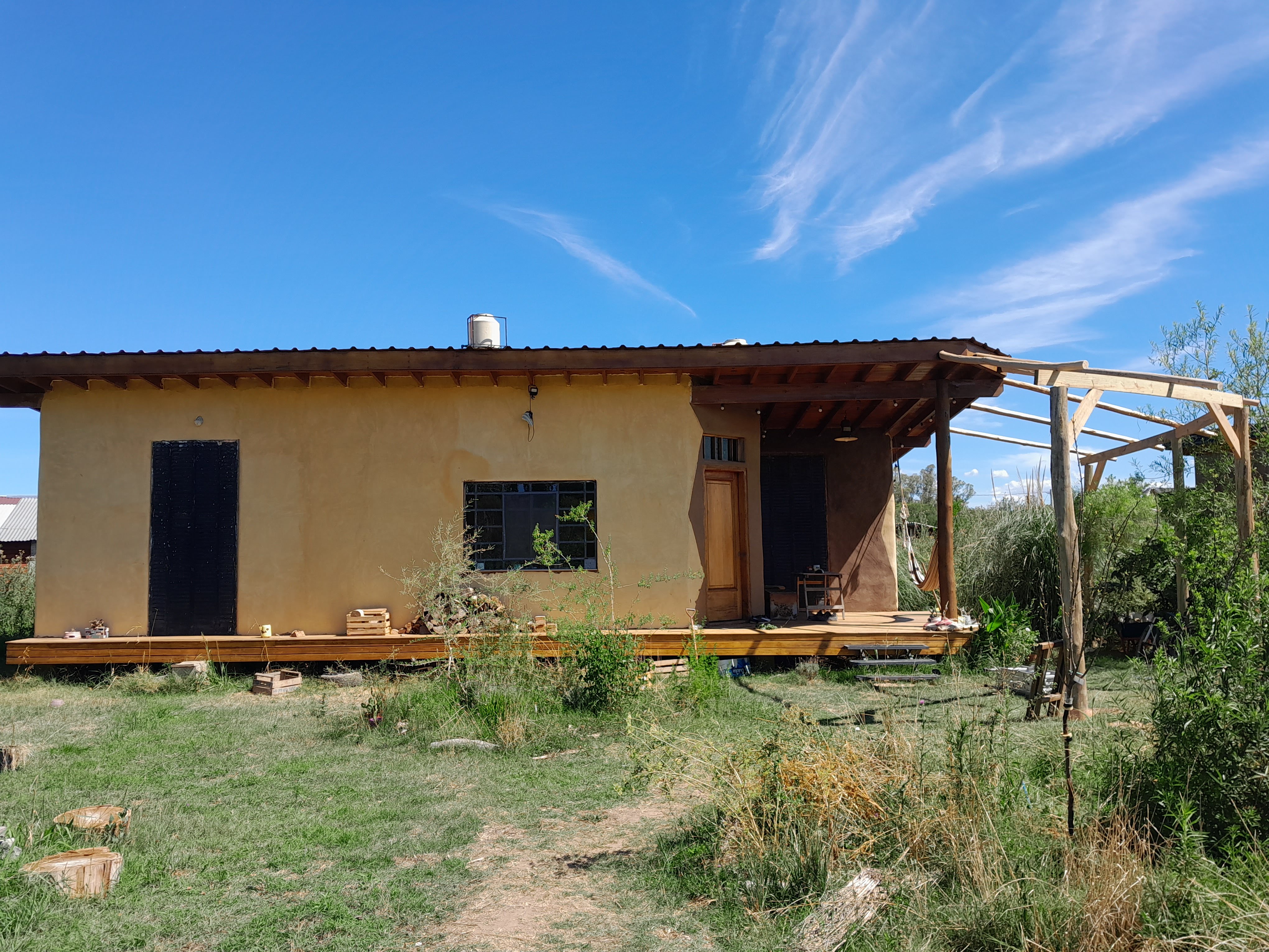 La imagen de una casa de color naranja en una tarima, rodeada de hierba y árboles, con un cielo claro azul.