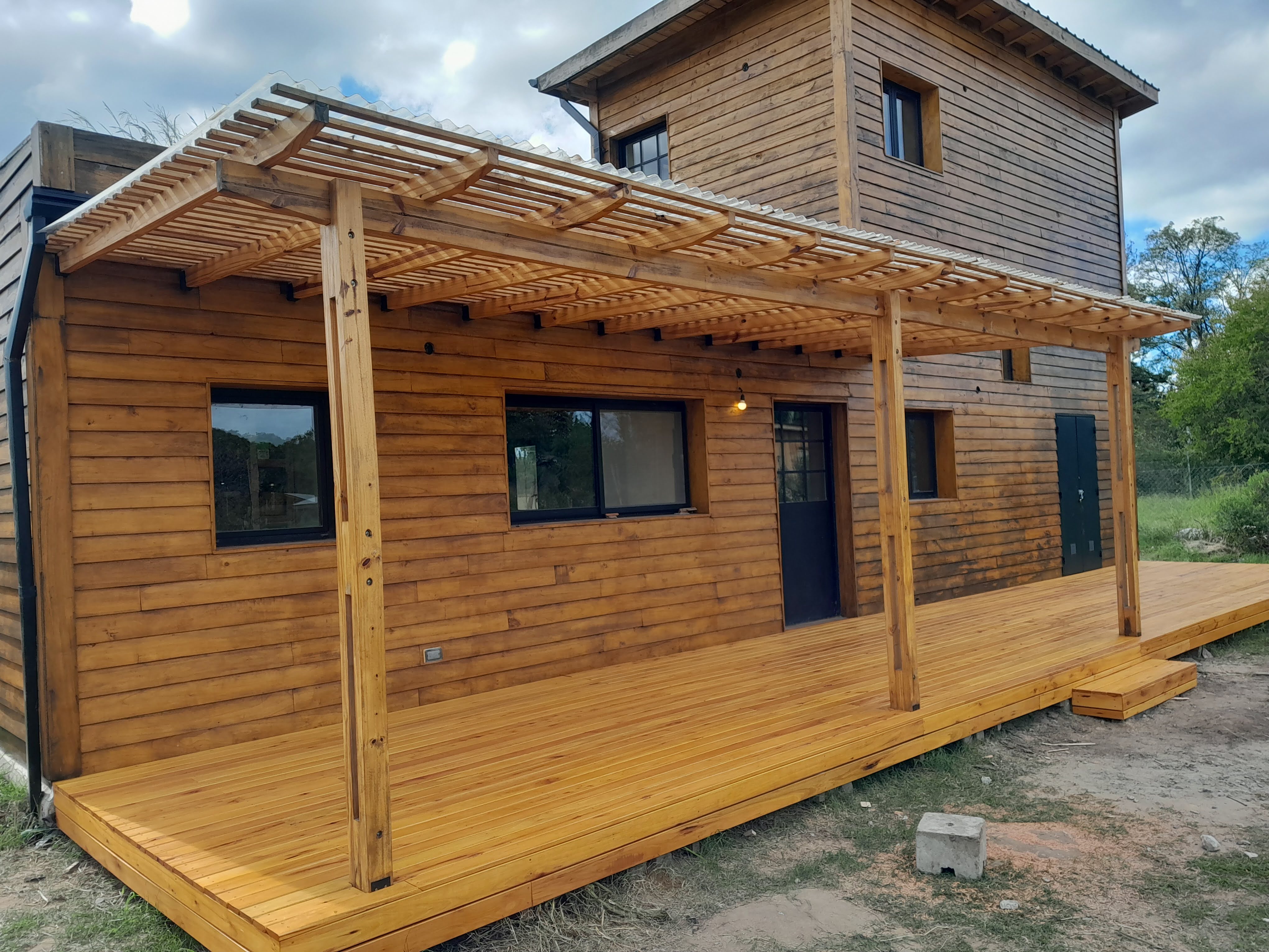 "Una casa de madera con una terraza y paredes de madera, con una empalizada." Translation: "A wooden house with a porch an...