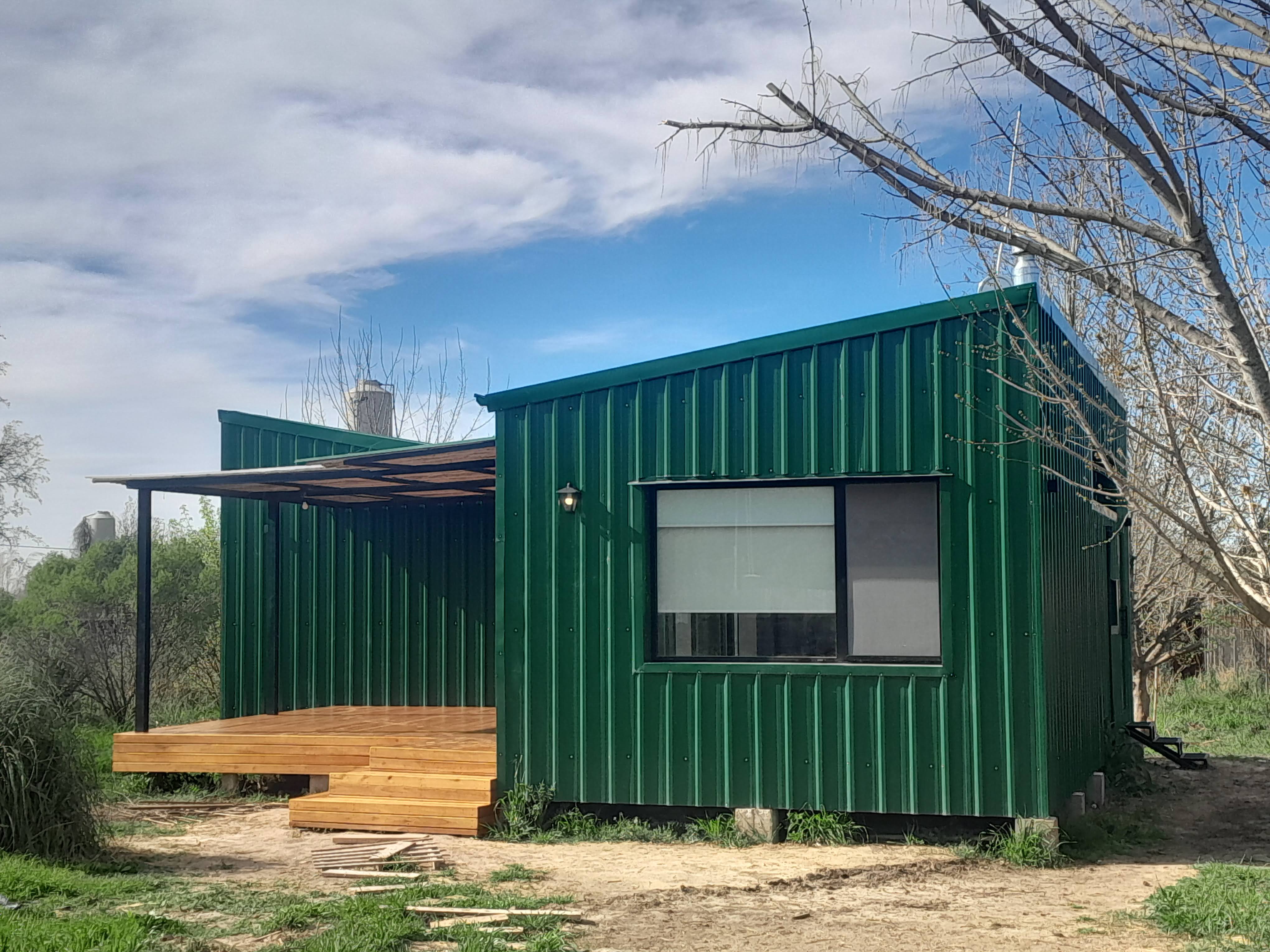 * The image depicts an isometric-facing frontal view of the outside wall of a green corrugated metal cabin. * The colors i...